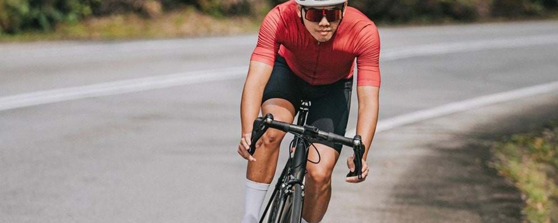 Cyclist wearing red jersey and white helmet riding a road bike on a curved road