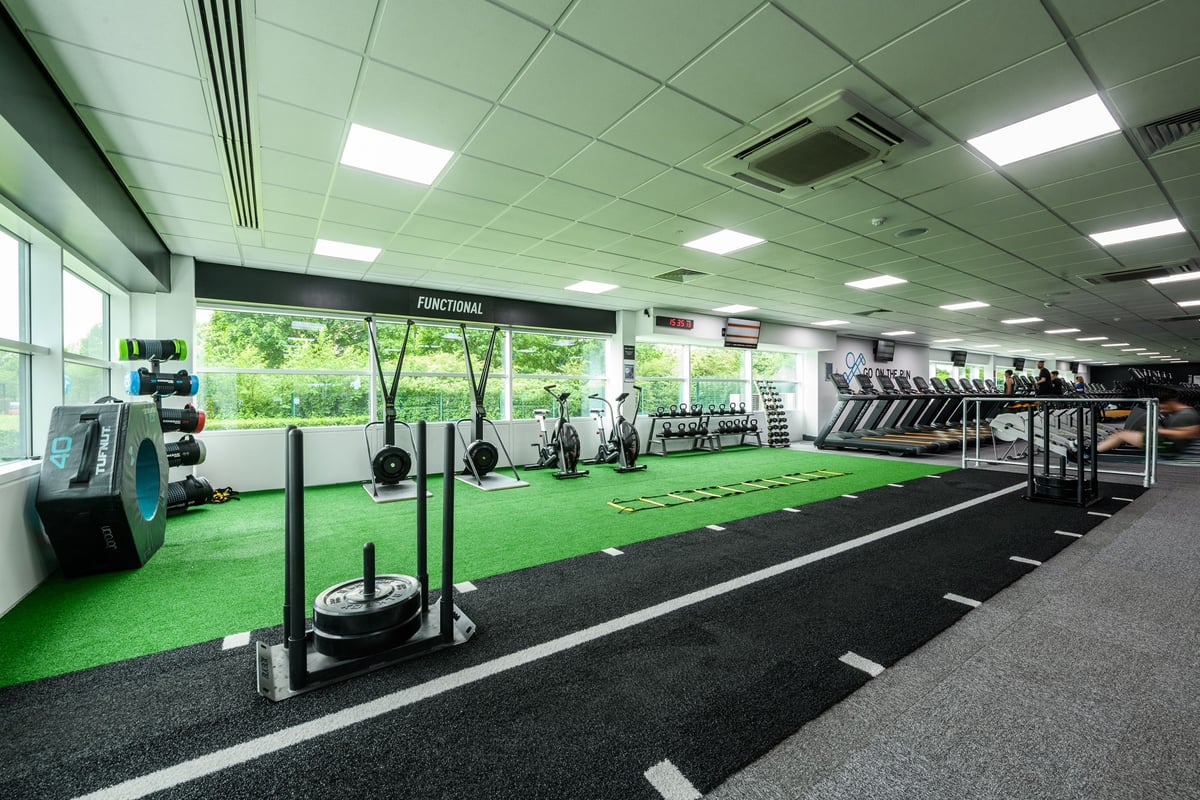 PureGym Newcastle Longbenton: Green turf workout area with squat racks, weight plates, benches, and resistance machines.