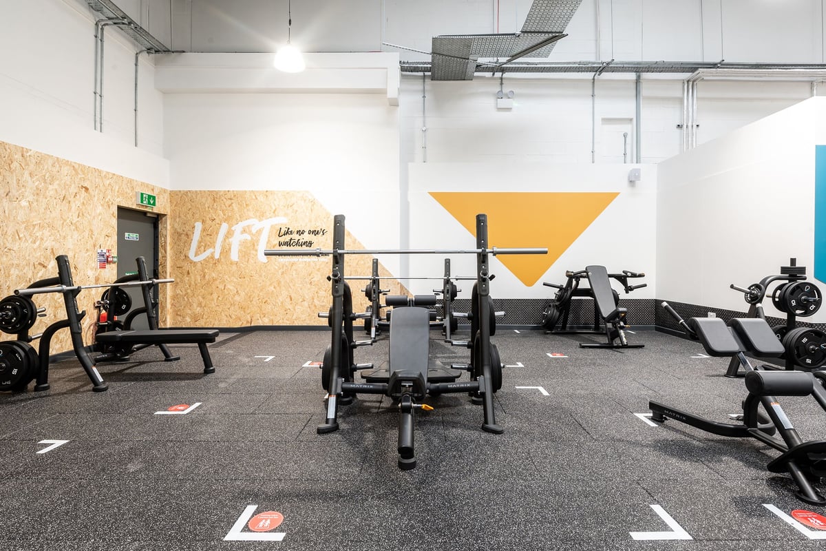 PureGym Stockport North: Squat racks, benches, weights, and rubberized gym flooring with geometric wall designs.