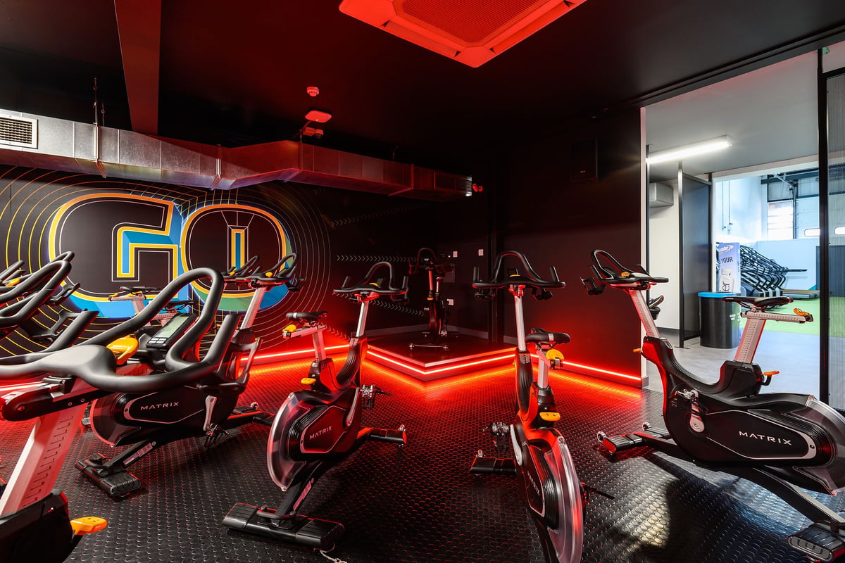 PureGym Reading Caversham Road: Rows of stationary bikes, neon lighting in red tones, and rubberized flooring.