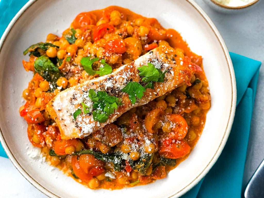 Grilled salmon on chickpea and spinach stew garnished with parsley and cheese