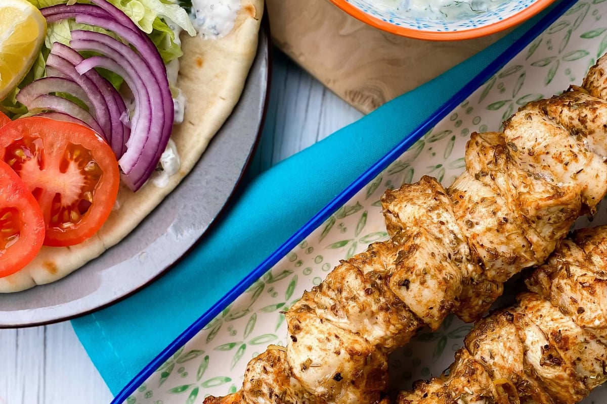 Grilled chicken skewers with flatbread topped with lettuce, tomato, onion, and tzatziki