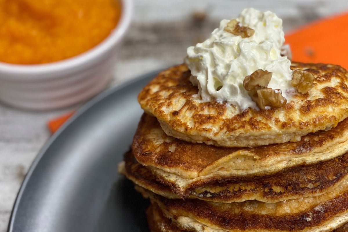 Stack of golden pancakes topped with cream and walnuts beside a bowl of pumpkin purée