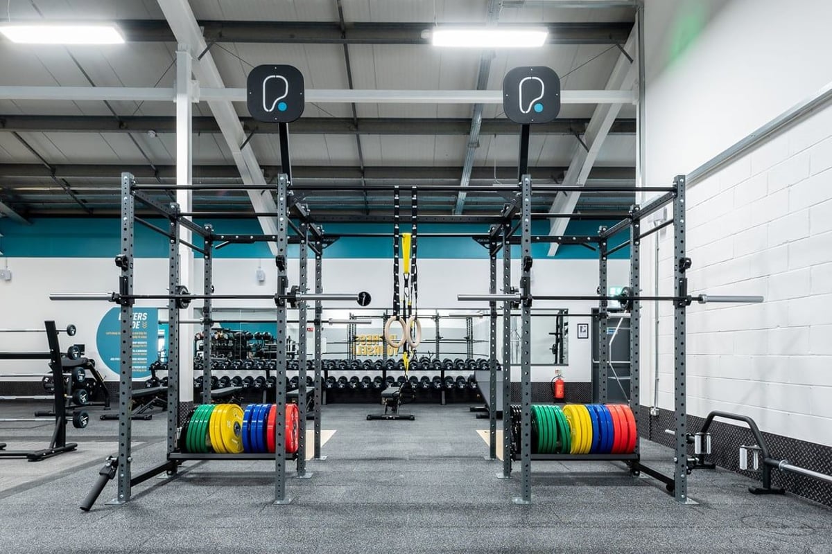 PureGym Uttoxeter: Squat racks, weight plates in various colours, rubberized flooring, and pull-up bars in a gym setting.