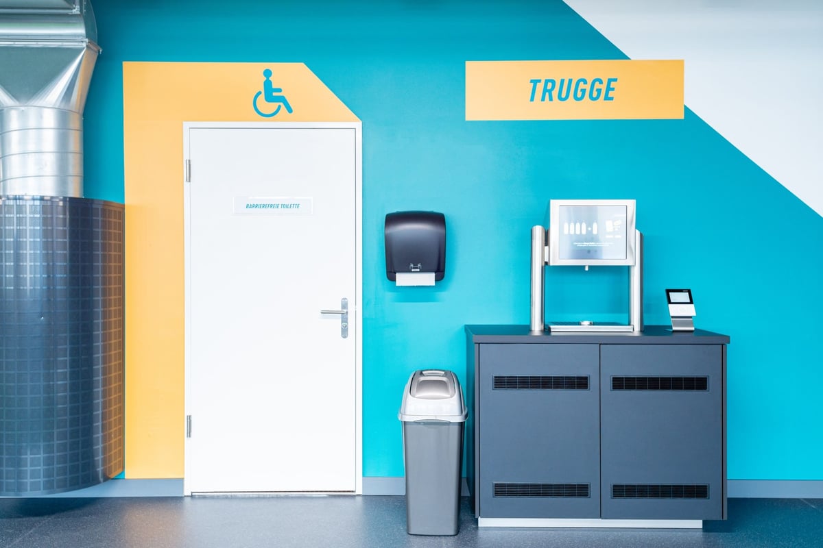 PureGym Altstetten: Ein Eingangsbereich mit Zugangstoren zum Fitnessstudio, Mülltonnen und einem