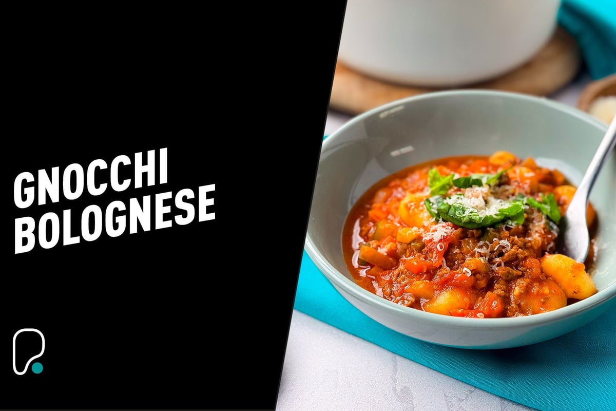 Bowl of gnocchi bolognese topped with grated cheese and basil leaves with a spoon inside