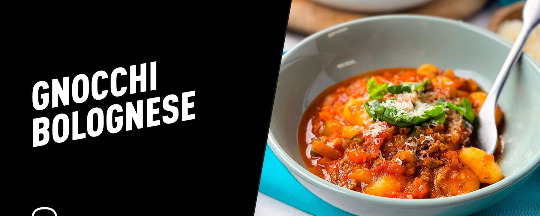 Bowl of gnocchi bolognese topped with grated cheese and basil leaves with a spoon inside