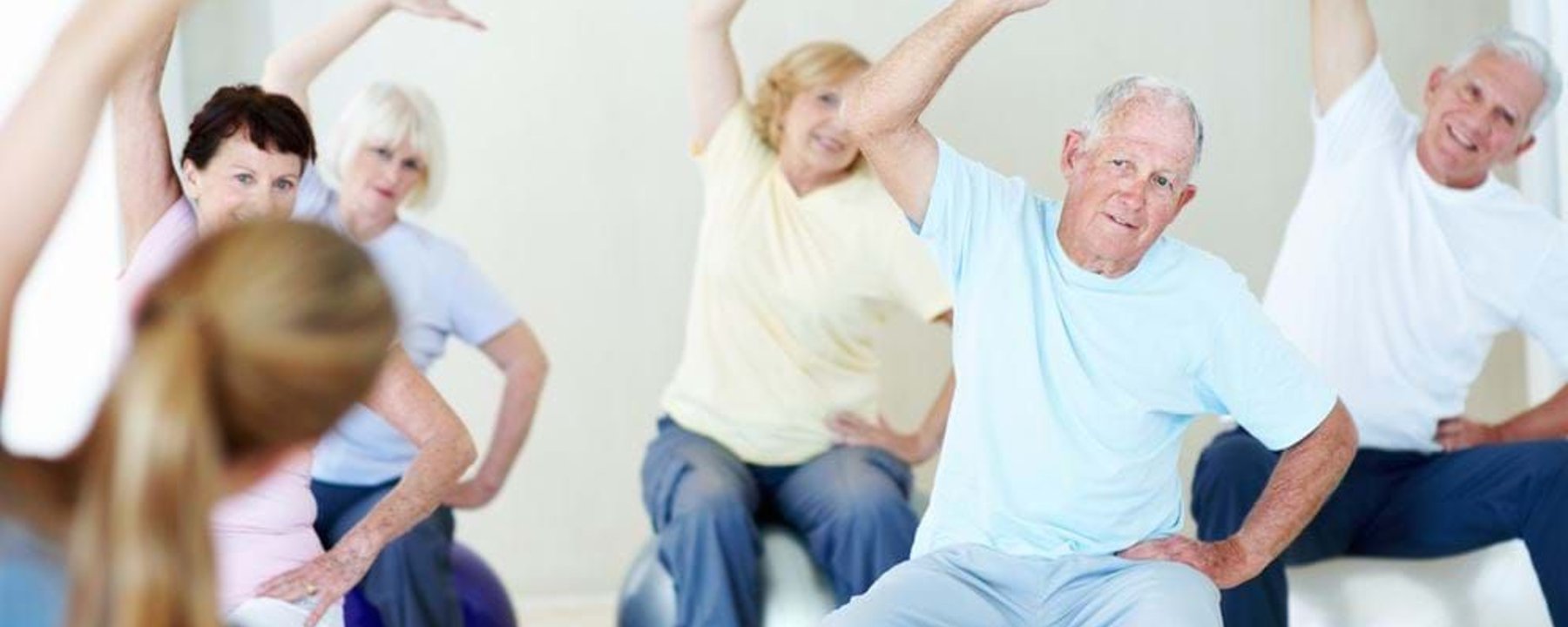 Seniors sitting on exercise balls stretching arms sideways in a fitness class.