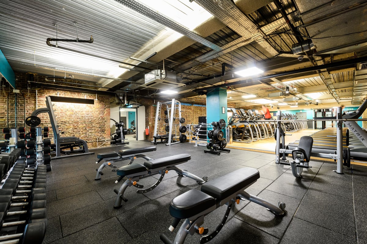 PureGym London Tower Hill: Bench presses, free weights and rubberised flooring with exposed brickwork and industrial ceiling.