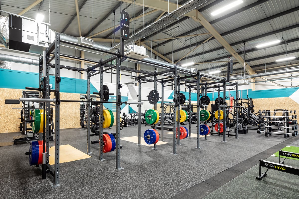 PureGym Neath: Squat racks, barbells, weight plates in various colours, and rubberized flooring within a gym setting.