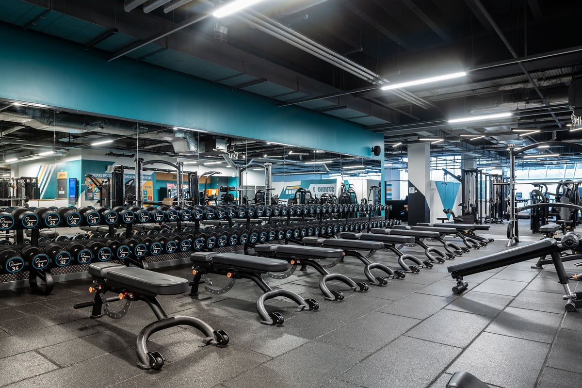 PureGym Ipswich Buttermarket: Rows of dumbbells, weight plates, benches and mirrored walls in a dimly lit gym.