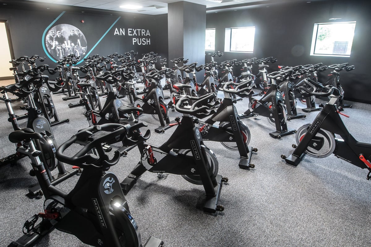 PureGym Denton: Rows of stationary cycles inside a dimly lit studio with motivational signage on the wall.