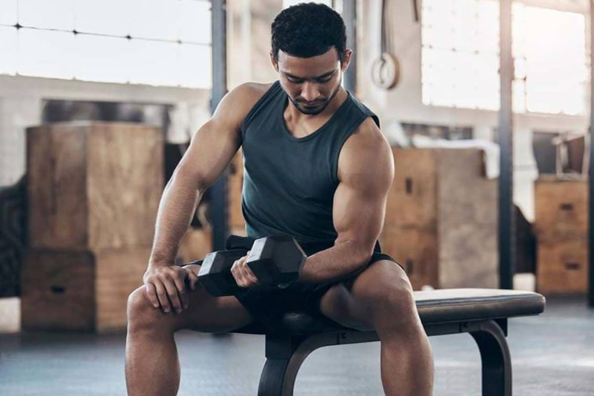 Mann sitzt auf Bank und hält Hantel in Fitnessstudio mit Backsteinwänden