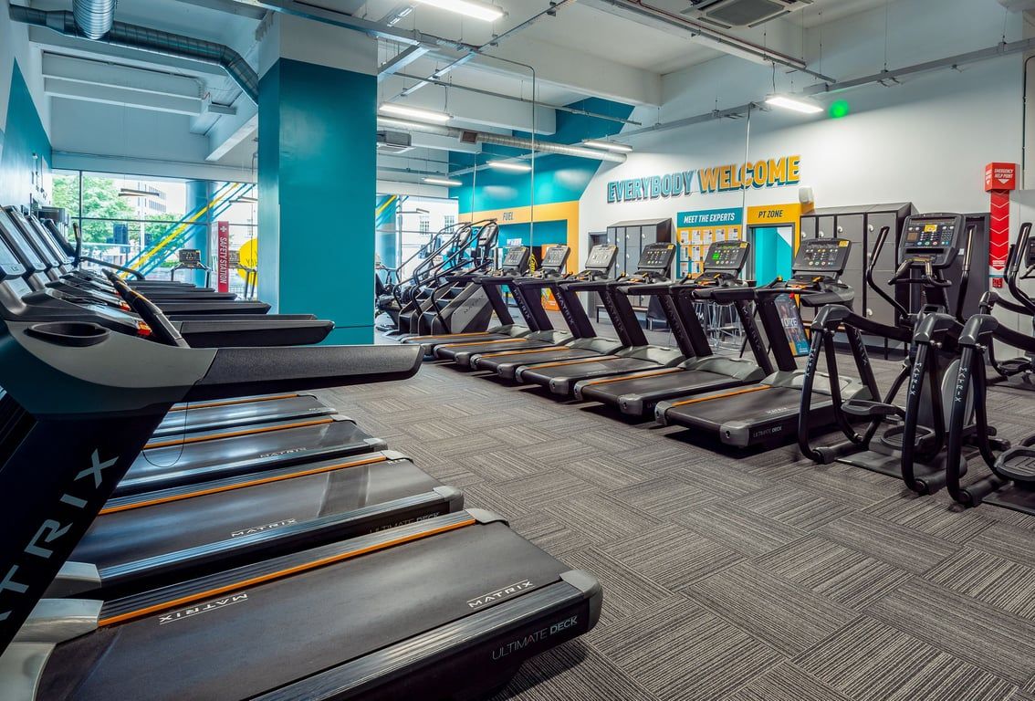 PureGym Leicester St Georges Way: Rows of treadmills, turquoise accents, and wall graphics in a bright fitness studio.