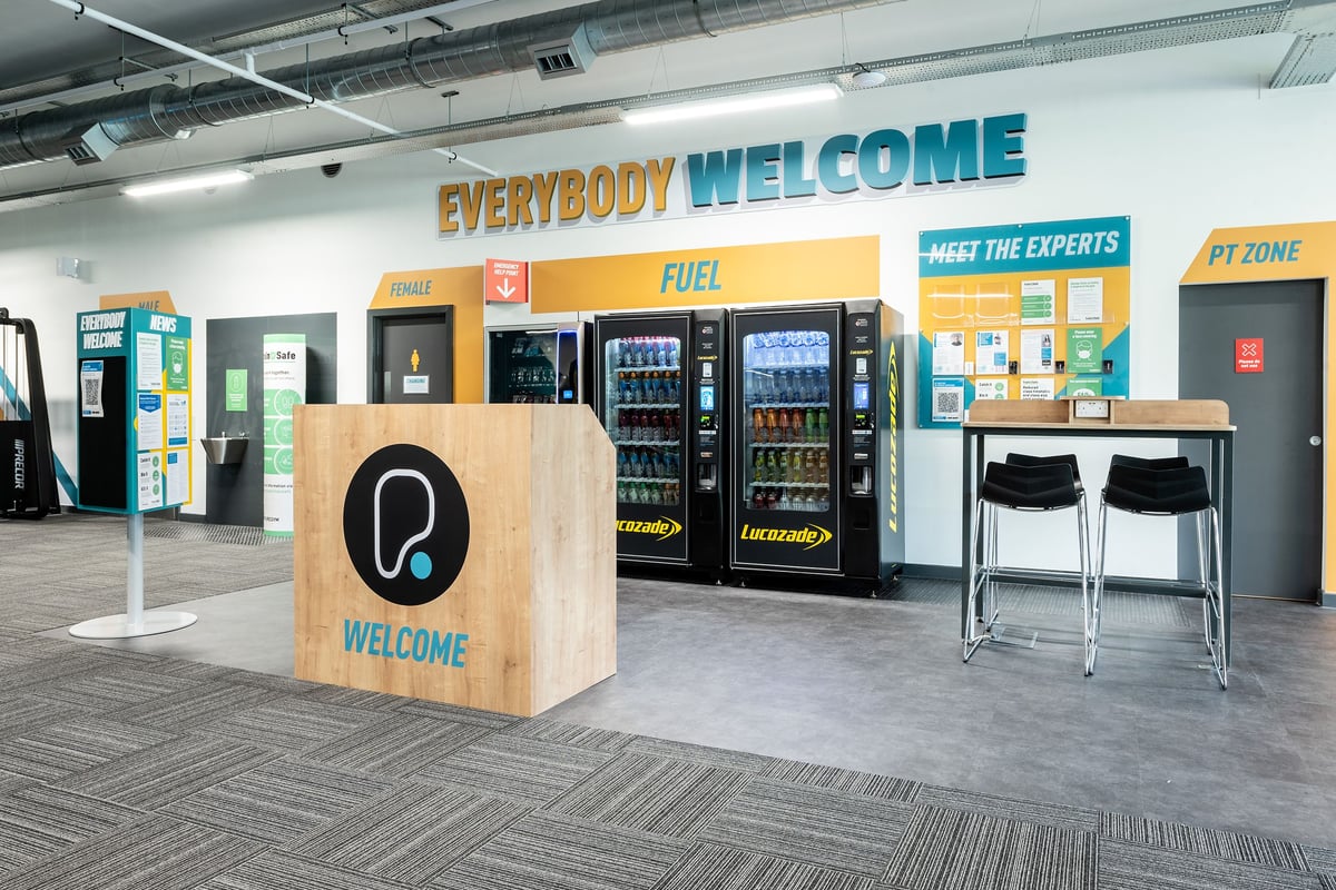 PureGym Witney: Vending machines, seating area, and fitness zone signage in a gym lobby.
