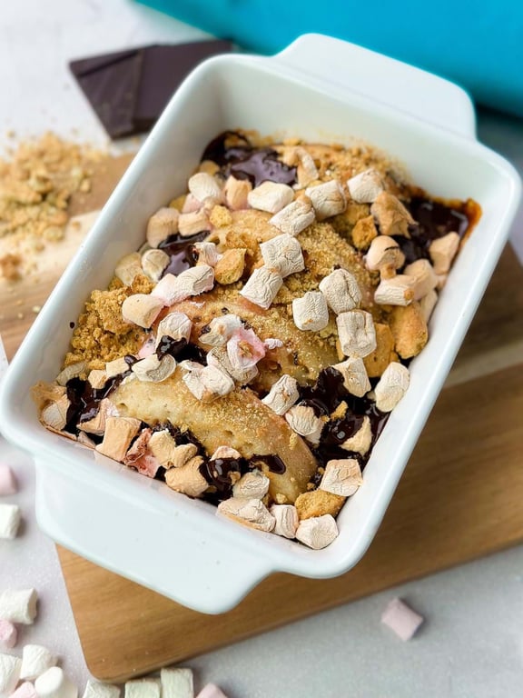 Baked dessert with marshmallows, chocolate sauce, and biscuit crumbs in a white dish