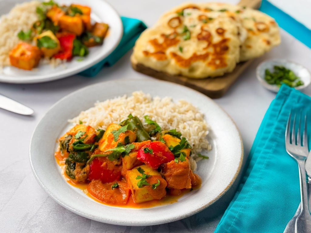 Plates of vegetable curry with rice and naan bread on a white table with turquoise napkins