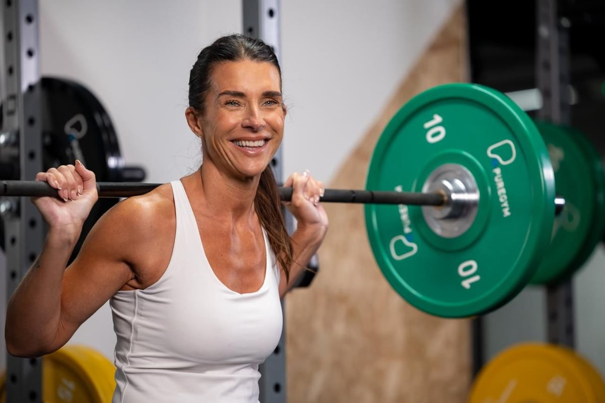 Smiling PureGym member holding a barbell on her shoulders