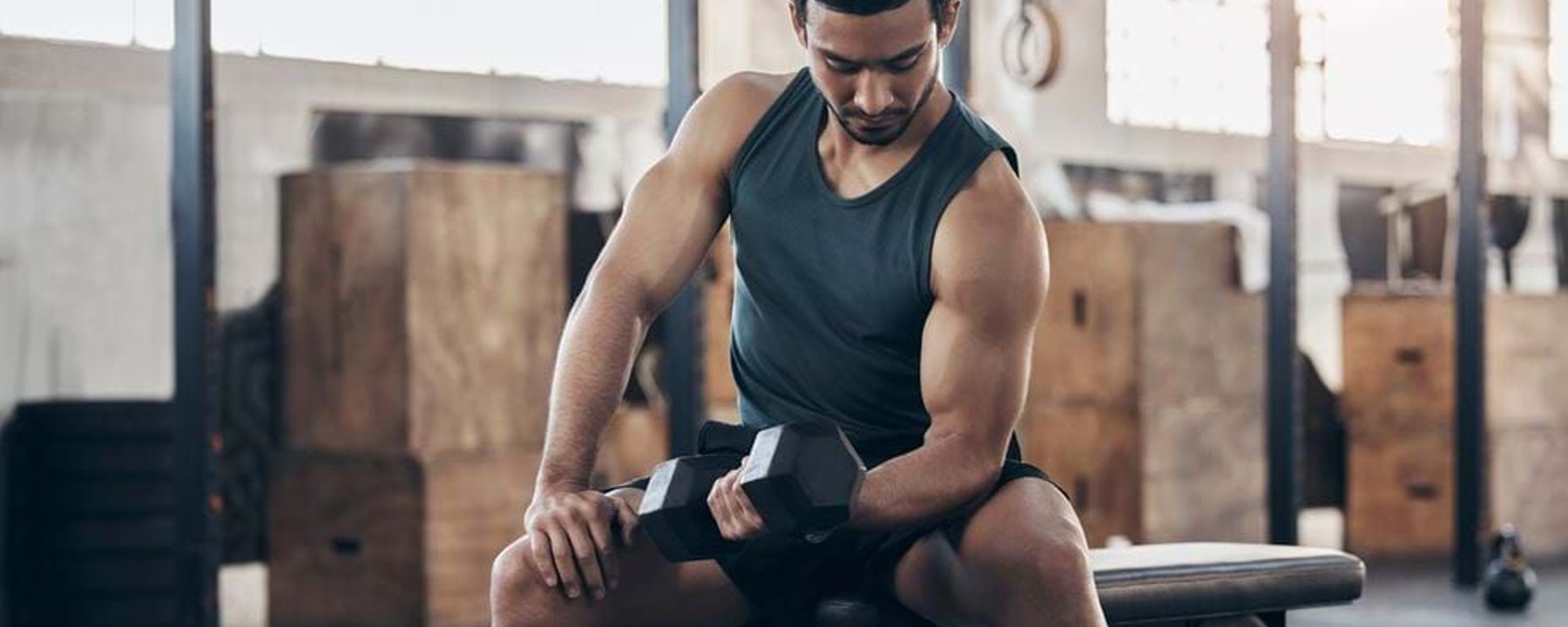 Man in black tank top lifting dumbbell while sitting on gym bench