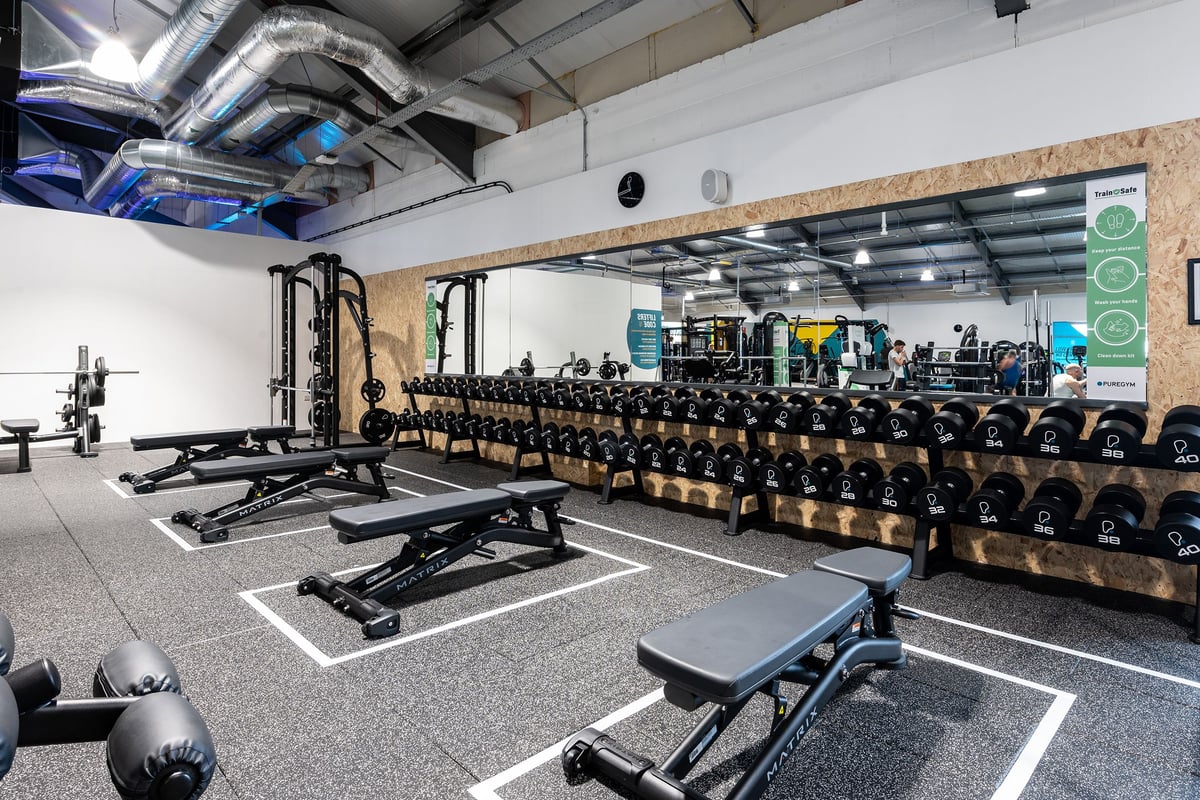 PureGym Stowmarket: Weightlifting area with squat racks, benches, dumbbells, weight plates, and rubberized floors.