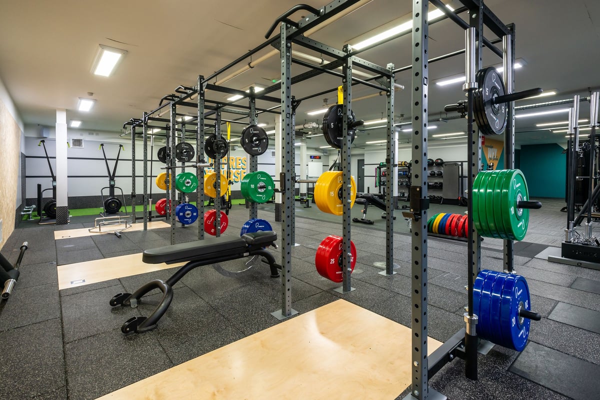 PureGym Wrexham: Rig of squat racks, weight plates in various colours, rubberized flooring, ropes, and kettlebells.