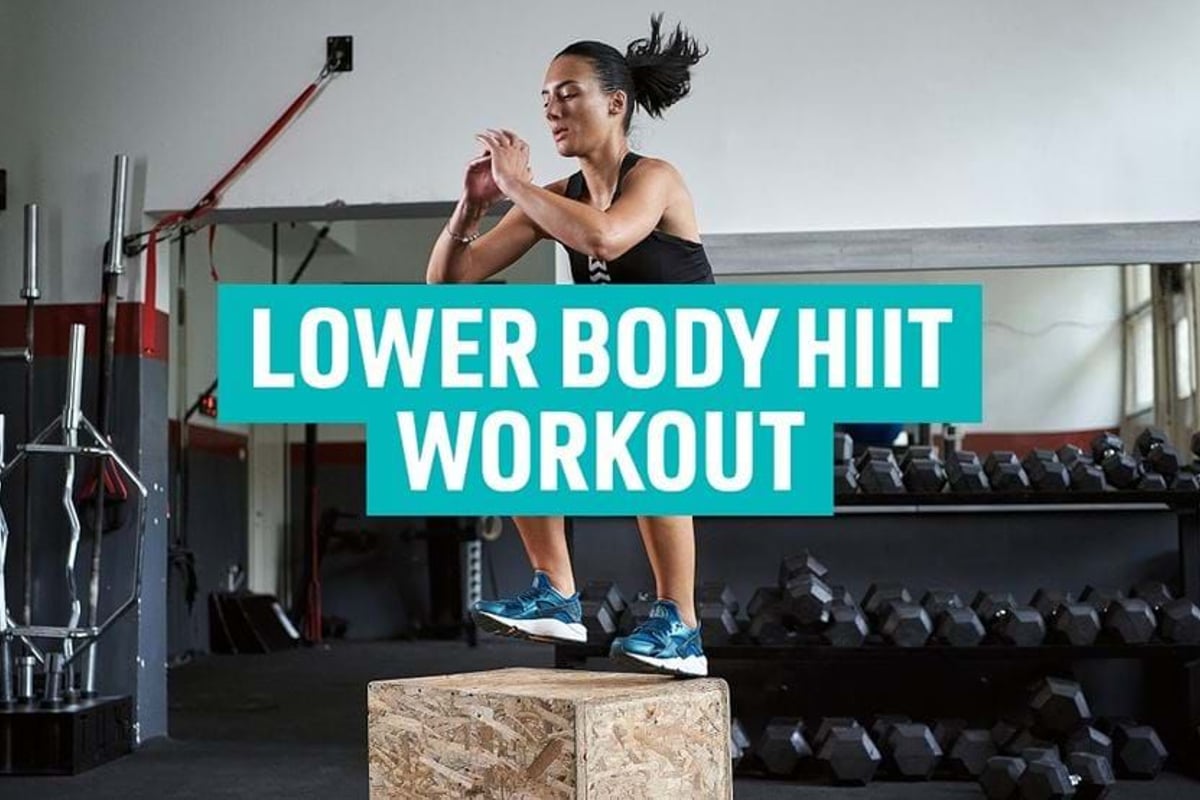 Woman jumping on wooden box in gym with dumbbells and barbells in background