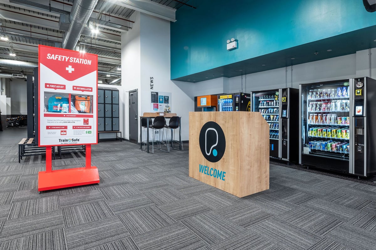 PureGym Newport Wales: Vending machines with drinks and snacks, a welcome desk, and a safety station sign.