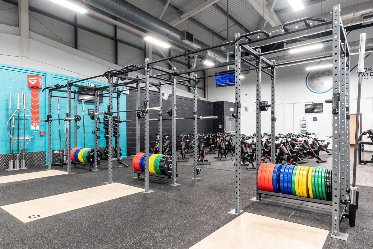 PureGym Birmingham West: Rig frames, weight plates of various hues, weight racks, rubberized flooring within a well-lit gym.