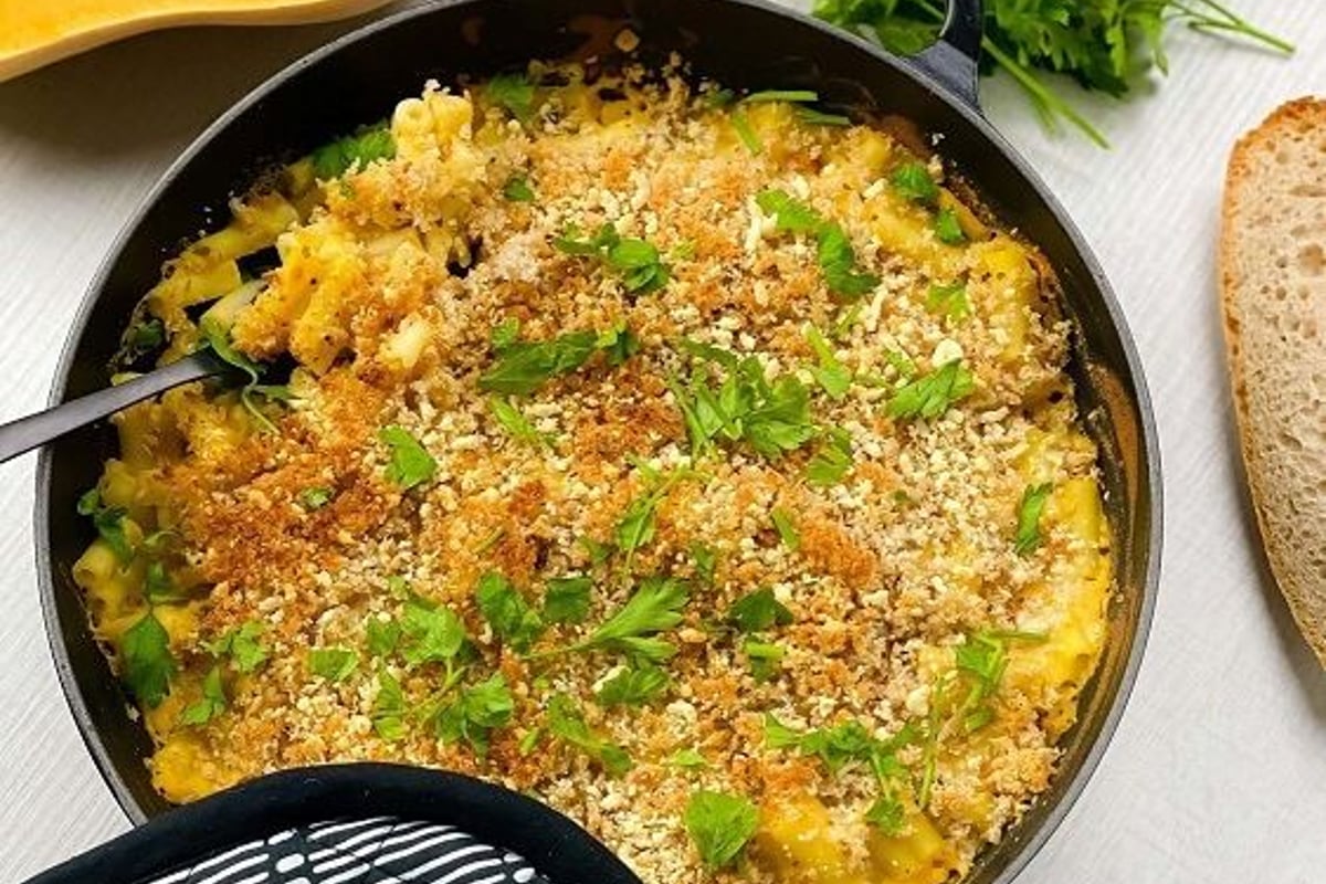 Baked macaroni and cheese with herb garnish in a black pan with pumpkin and bread nearby