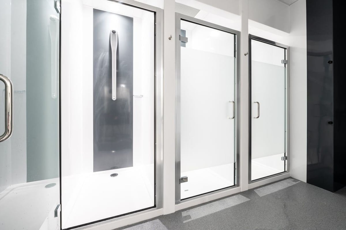 PureGym Aldershot Westgate Retail Park: Rows of glass-enclosed shower stalls or changing rooms with benches.