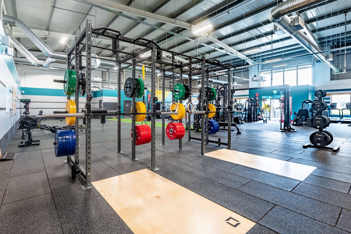 PureGym Stamford: Rig with weights, benches, rubberized flooring, mirrors in gym setting.
