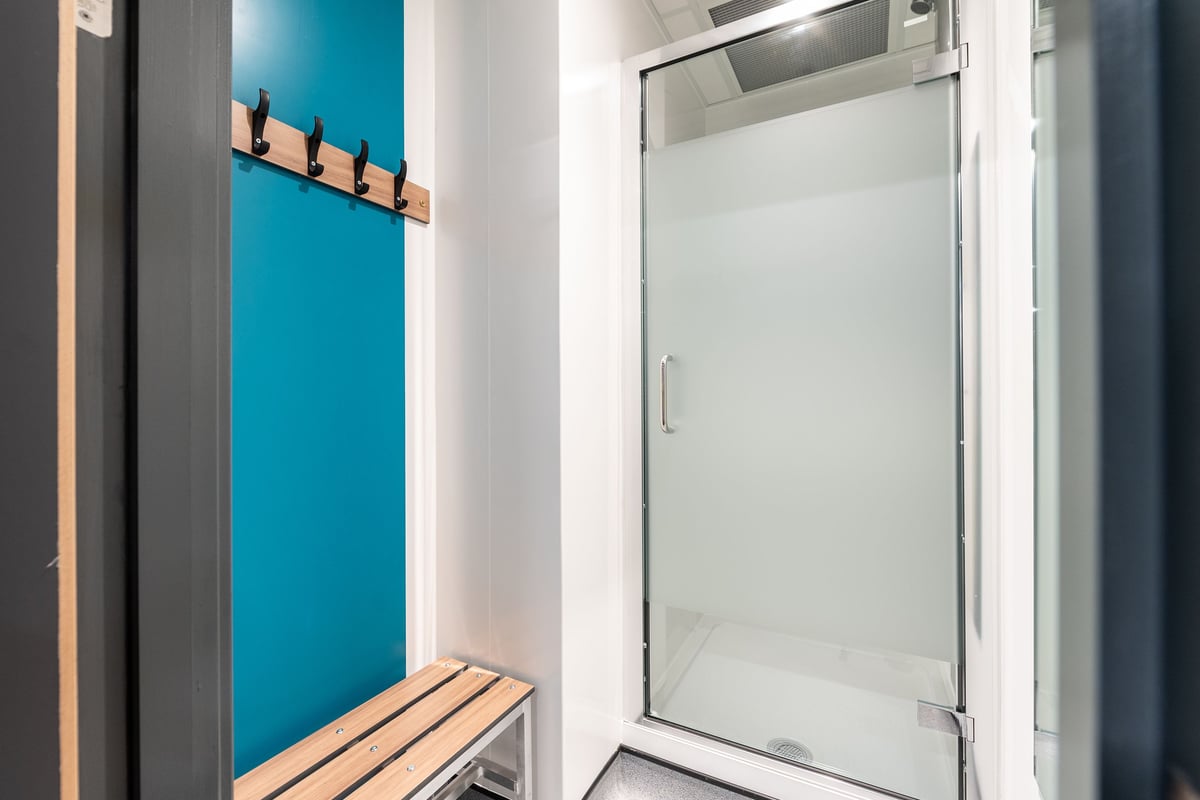 PureGym Droitwich Spa: Teal accent wall, wooden bench seating, shower stall with glass door.