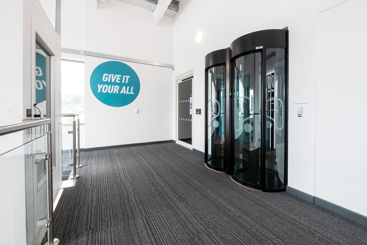 PureGym Portsmouth North Harbour: Glass entry gates, grey flooring, motivational signage "Give It Your All" on wall.