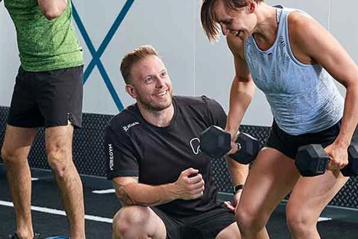 Fitnesstrainer in schwarzem Shirt zeigt Gruppe beim Trainieren eine Übung