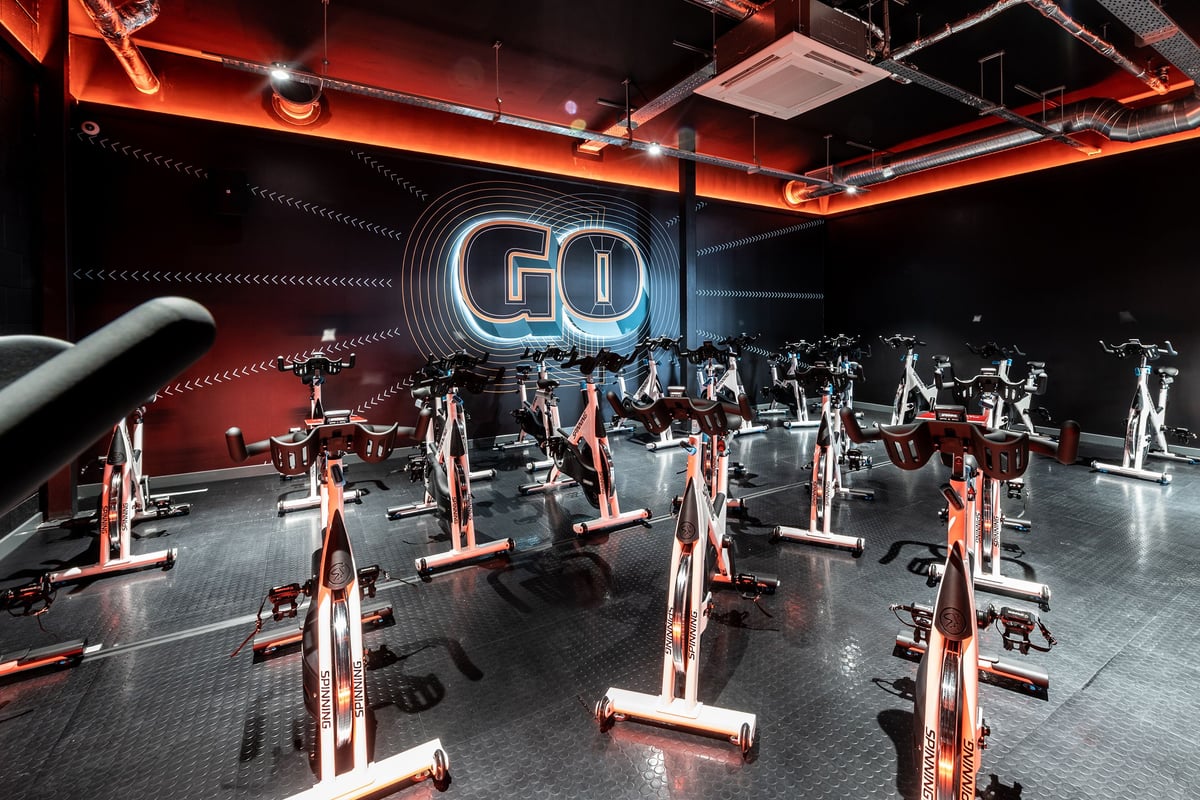 PureGym Bournemouth Mallard Road Retail Park: Rows of stationary bikes, free weights, and neon "GO" sign in red-lit studio.