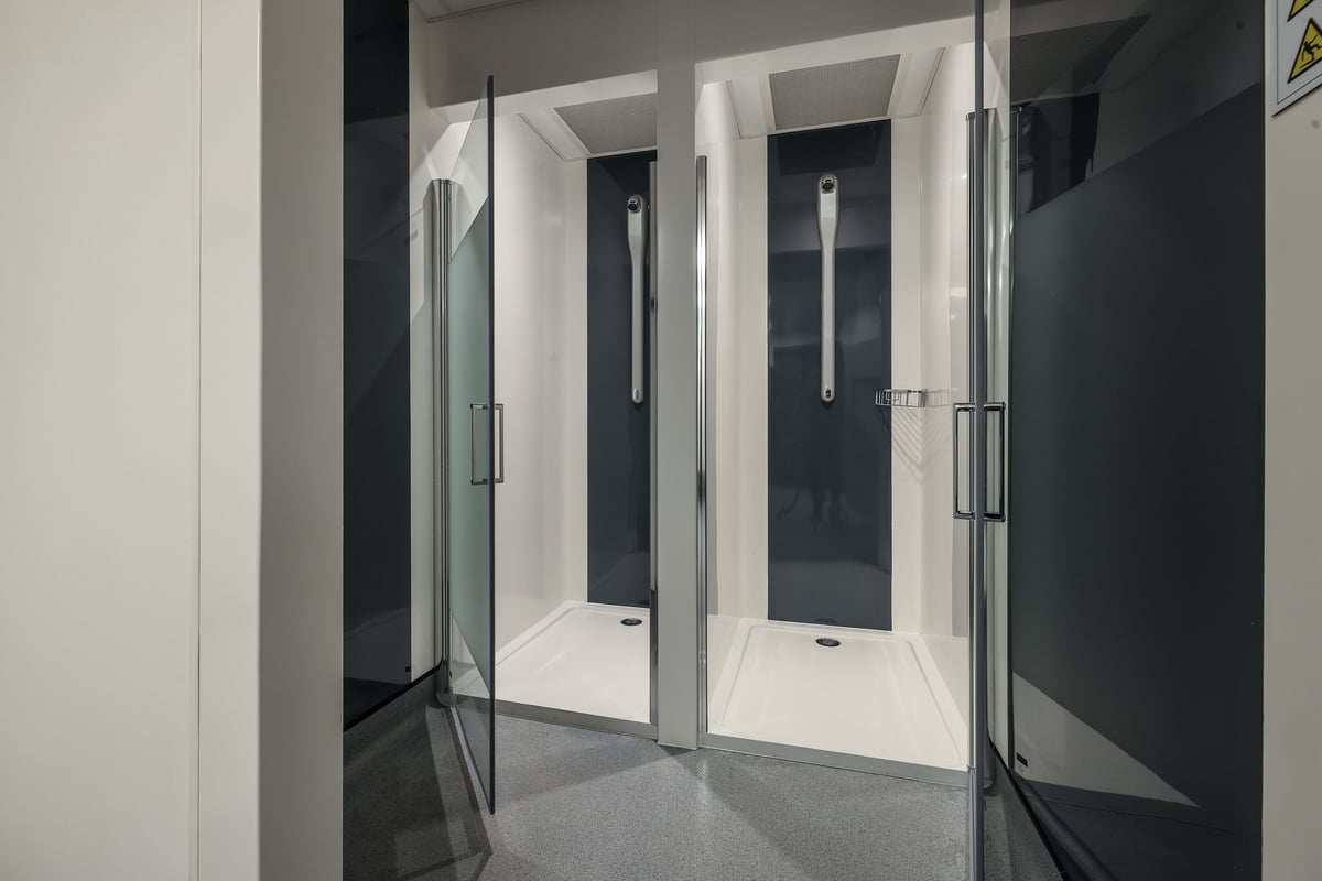 PureGym Bishop Auckland: Shower stalls with glass doors and gray tiled flooring.