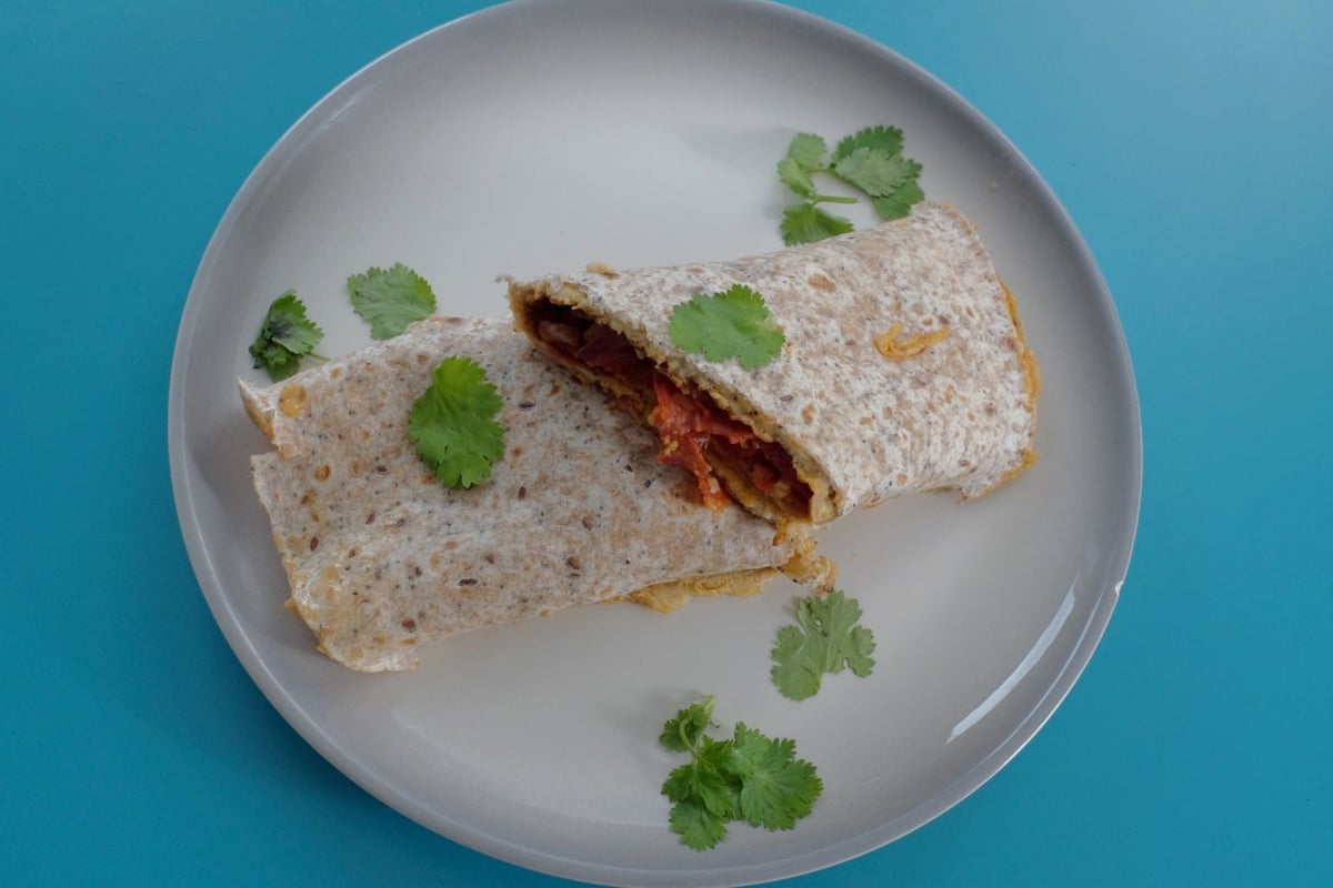 Wholemeal wrap filled with chorizo and egg on grey plate with coriander garnish