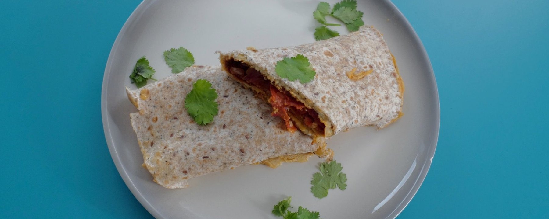 Wholemeal wrap filled with chorizo and egg on grey plate with coriander garnish