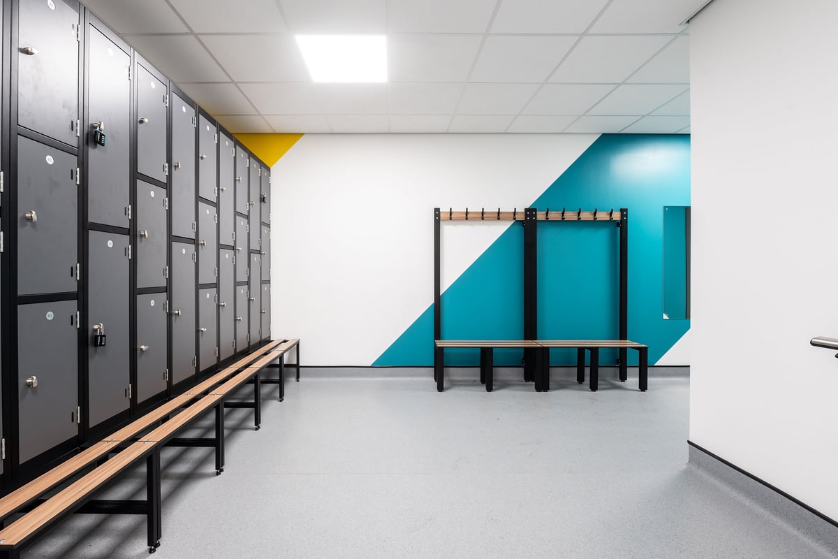 PureGym Craigavon: Lockers, benches, and a padded wall partition in a changing room setting.