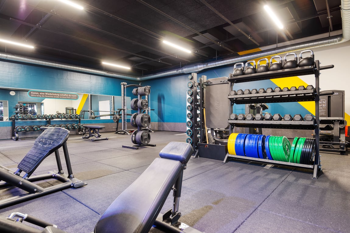 PureGym Aarau: Illuminazione al neon, testo motivazionale sulla parete e passerella curva all'interno di una palestra dai colori scuri.