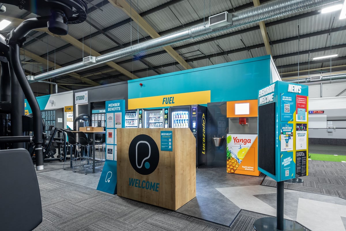 PureGym Neath: Welcome kiosks, fuel signage, seating, and vending machines.