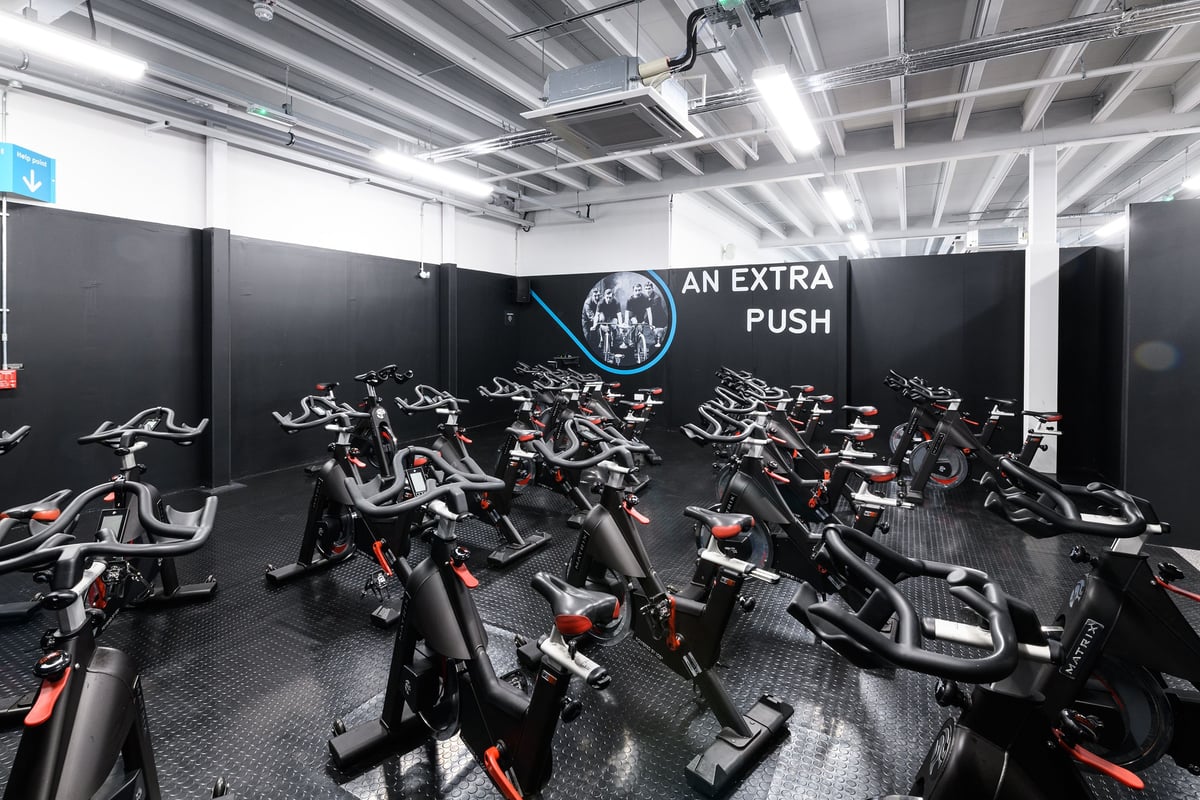 PureGym Aberdeen Wellington Circle: Rows of stationary bikes in a dimly lit studio with mirrored walls and sleek black decor.
