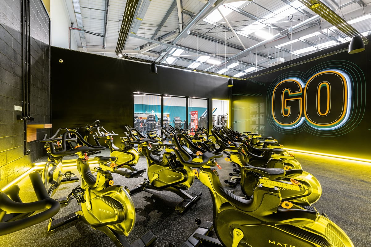 PureGym Broadstairs Westwood Gateway Retail Park: Rows of stationary bikes in a dimly-lit studio with neon signage.
