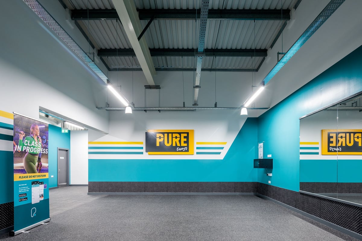 PureGym Frome: Reception area with teal walls, dark flooring, bench seating, and "PURE" signage.