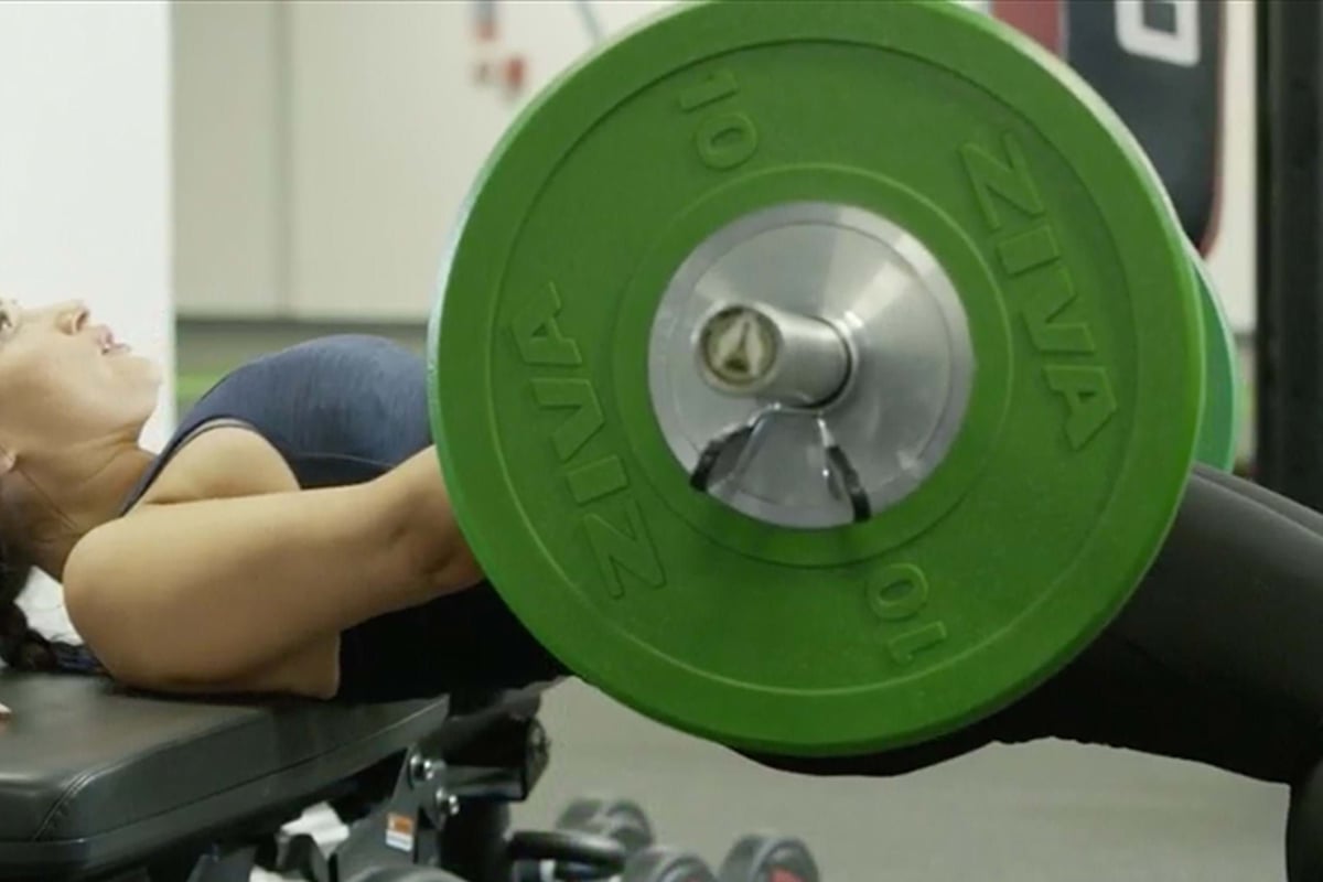 Woman performing hip thrust exercise with a barbell in a gym setting