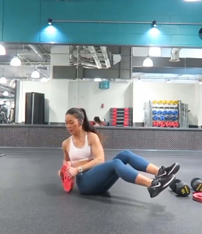 Woman in sportswear doing Russian twists with a red weight plate in a gym