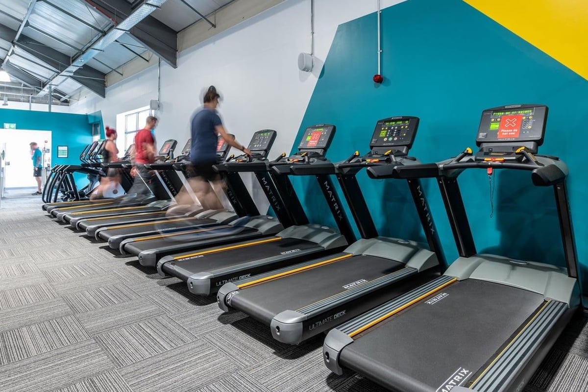 PureGym Stowmarket: Rows of treadmills with monitors in a colourful gym setting.