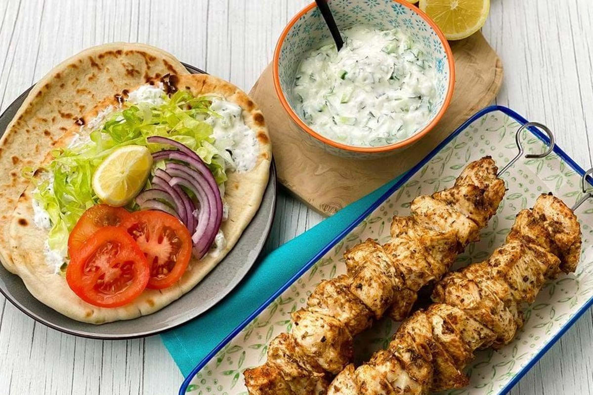 Grilled chicken skewers with flatbread, sliced tomato, onion, lettuce, lemon, and sauce