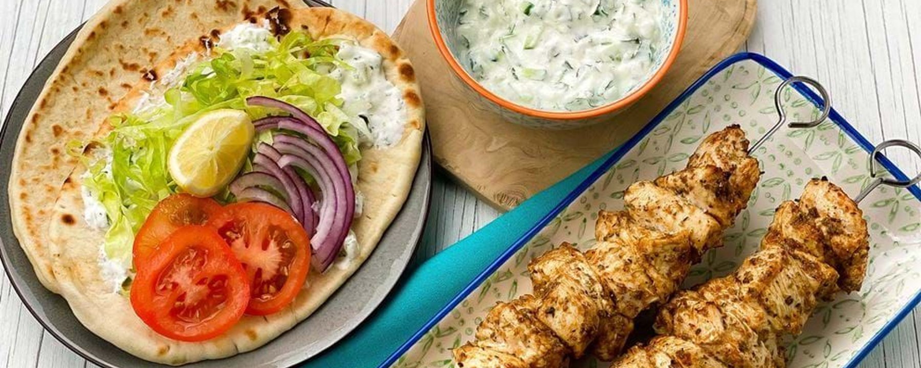Grilled chicken skewers with flatbread, sliced tomato, onion, lettuce, lemon, and sauce