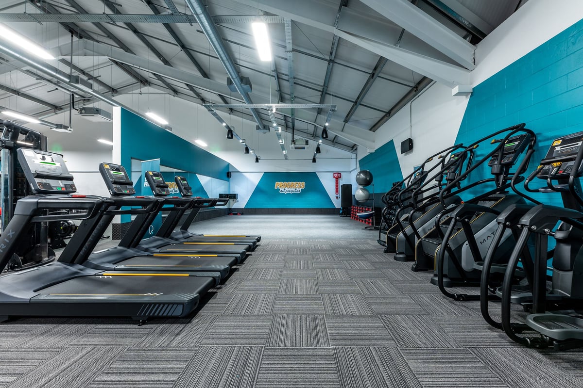 PureGym Uttoxeter: Row of treadmills, cross-trainers, and stationary bikes in a gym with teal accents.